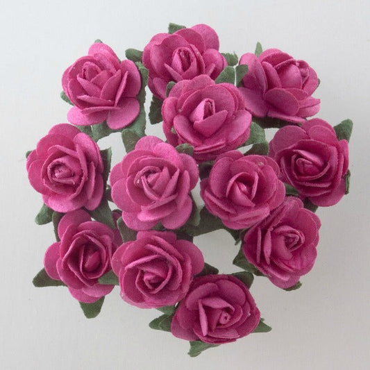 A top view of a bouquet of twelve fuchsia paper tea roses with green leaves, arranged in a circular pattern against a light gray background. The vibrant roses are in full bloom, perfect for crafting projects like Paper Tea Rose Flower Stems or elegant card making. This lovely bunch, known as the Fuchsia Paper Tea Roses Bunch of 12 by Perfect Tables, adds a touch of elegance to any DIY project.