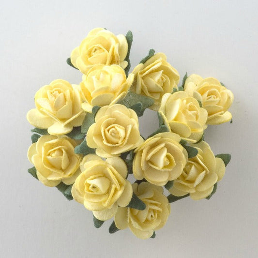 A cluster of Lemon Paper Tea Roses Bunch of 12 from Perfect Tables, featuring soft, delicate petals and green leaves with visible stems, are arranged in a circular formation on a light, neutral background. These small, pale yellow roses have a slightly curled texture, making them perfect for craft projects.