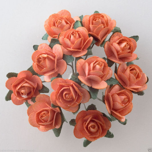 A bunch of vibrant orange-colored artificial roses, perfect for craft projects, are arranged in a circular bouquet with green leaves. Featuring intricate petal details, these Orange Paper Tea Roses by Perfect Tables are set against a plain background to showcase their vivid color and delicate craftsmanship.