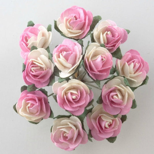 A close-up of the Pink and Cream Paper Tea Roses Bunch of 12 by Perfect Tables, featuring a dozen artificial roses with a blend of pink and white petals. Each rose is meticulously crafted to resemble detailed paper tea roses with green leaves, arranged neatly in an elegant circular pattern. The plain white background accentuates the vibrant colors, making them perfect for potential craft projects.