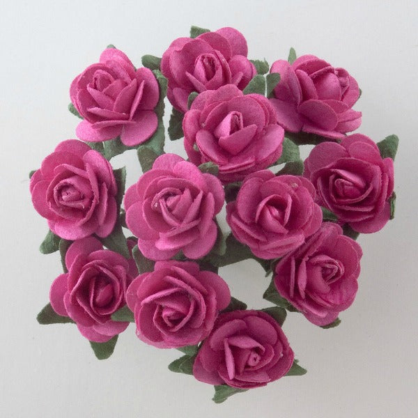 A top view of a bouquet of twelve fuchsia paper tea roses with green leaves, arranged in a circular pattern against a light gray background. The vibrant roses are in full bloom, perfect for crafting projects like Paper Tea Rose Flower Stems or elegant card making. This lovely bunch, known as the Fuchsia Paper Tea Roses Bunch of 12 by Perfect Tables, adds a touch of elegance to any DIY project.